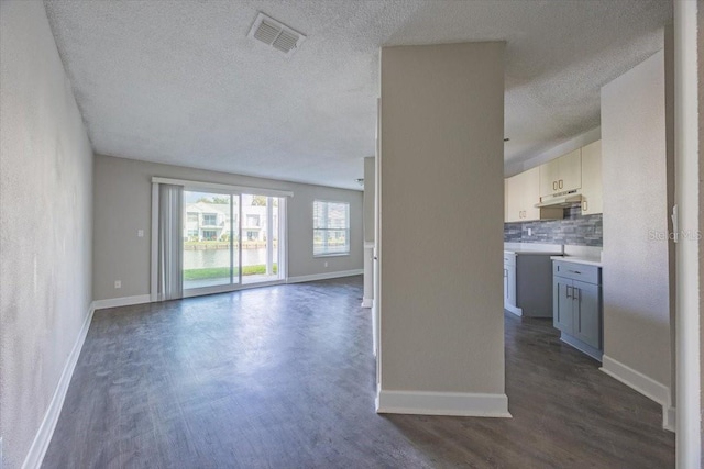 unfurnished living room featuring dark wood-style floors, visible vents, a textured ceiling, and baseboards