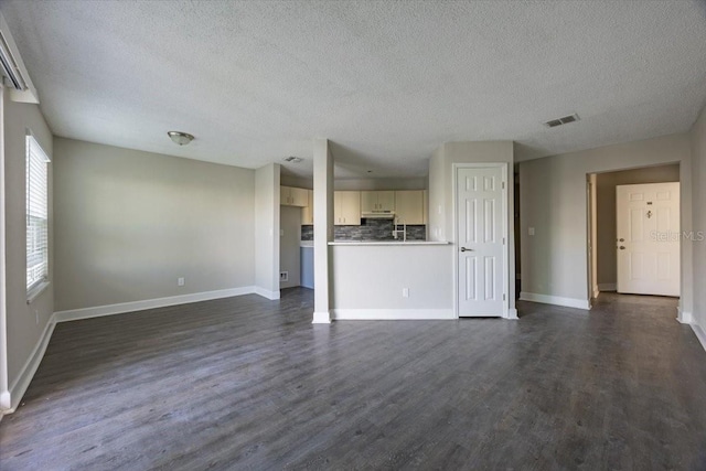 unfurnished living room featuring visible vents, dark wood finished floors, a textured ceiling, and baseboards