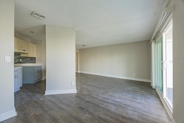 unfurnished living room featuring visible vents, a textured ceiling, baseboards, and dark wood-type flooring