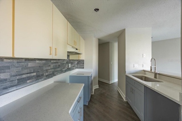 kitchen featuring under cabinet range hood, a sink, light stone countertops, tasteful backsplash, and dark wood finished floors