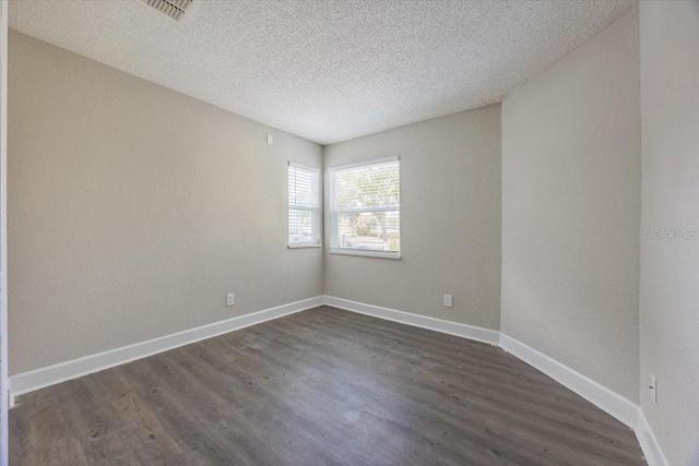 unfurnished room featuring dark wood-style floors, a textured ceiling, visible vents, and baseboards