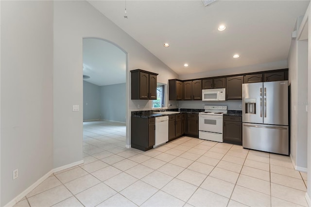 kitchen featuring dark brown cabinetry, white appliances, baseboards, lofted ceiling, and light tile patterned flooring