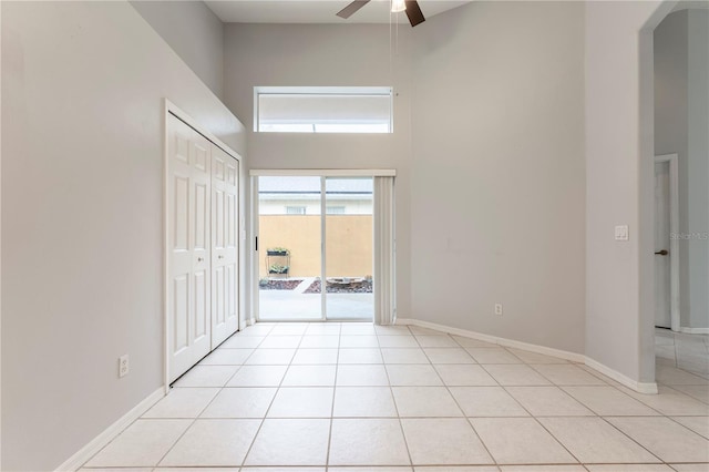 spare room featuring light tile patterned floors, arched walkways, a high ceiling, a ceiling fan, and baseboards