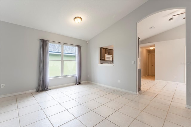 empty room with arched walkways, light tile patterned flooring, vaulted ceiling, and baseboards