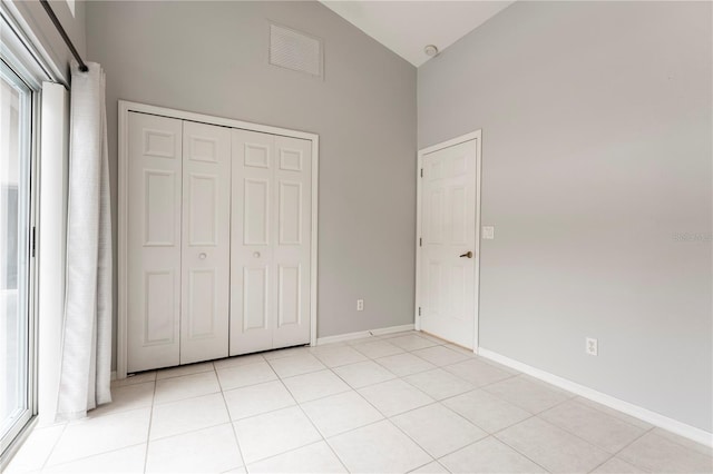 unfurnished bedroom with light tile patterned floors, baseboards, visible vents, high vaulted ceiling, and a closet