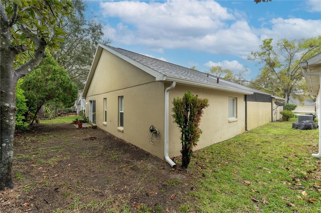 view of side of home with a shingled roof, a lawn, and stucco siding