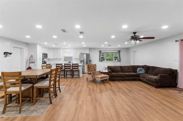 living room with light wood-style flooring, a ceiling fan, visible vents, and recessed lighting