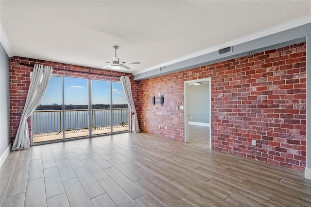 spare room featuring a ceiling fan, visible vents, a textured ceiling, and brick wall