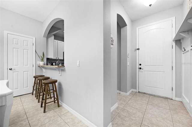 foyer with arched walkways, light tile patterned flooring, and baseboards