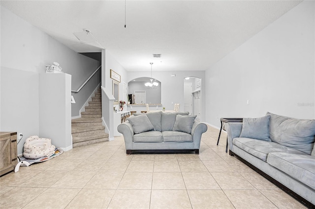 living room with arched walkways, light tile patterned flooring, visible vents, baseboards, and stairs