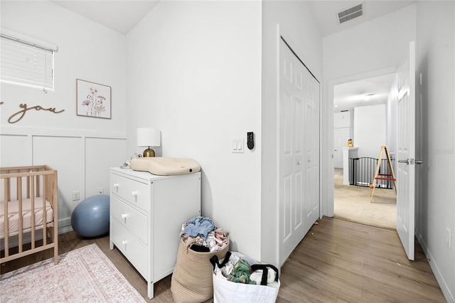 bedroom featuring a closet, visible vents, a decorative wall, wood finished floors, and a nursery area