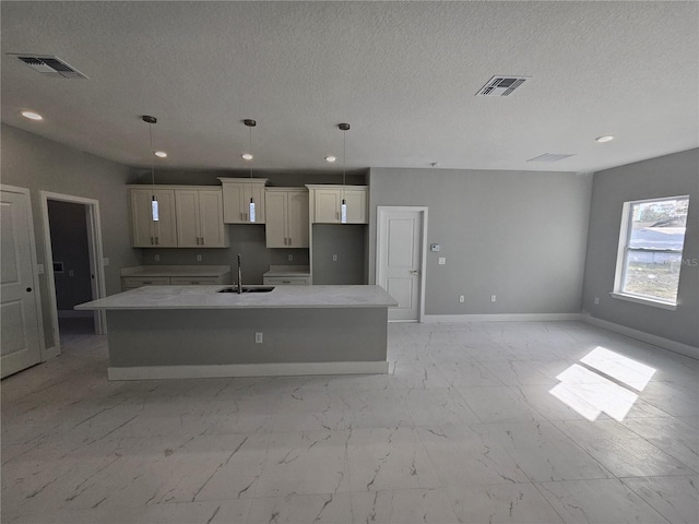 kitchen with a kitchen island with sink, marble finish floor, visible vents, and a sink