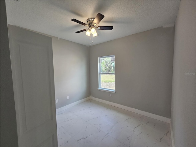 unfurnished room with marble finish floor, ceiling fan, a textured ceiling, and baseboards