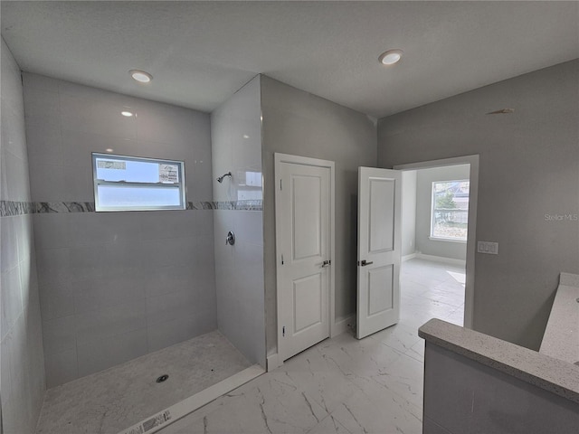 bathroom featuring marble finish floor, baseboards, a tile shower, and recessed lighting