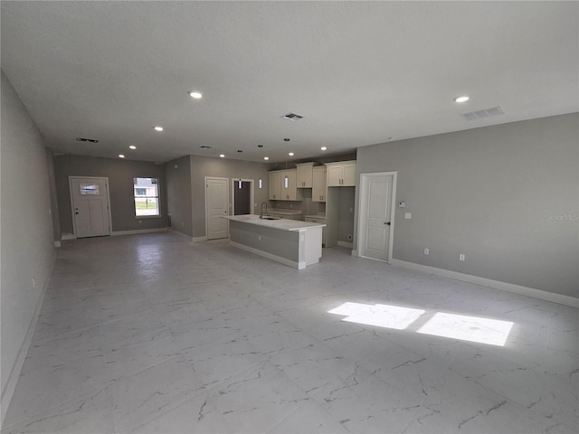 unfurnished living room featuring marble finish floor, a sink, visible vents, and baseboards