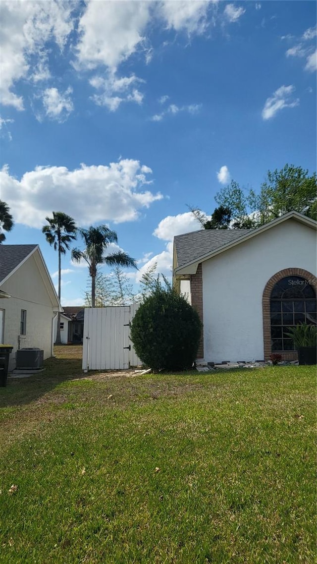 view of side of property featuring stucco siding, a shingled roof, central AC, and a yard