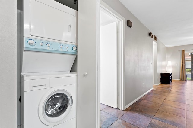 washroom with stacked washer and dryer, tile patterned floors, laundry area, and baseboards