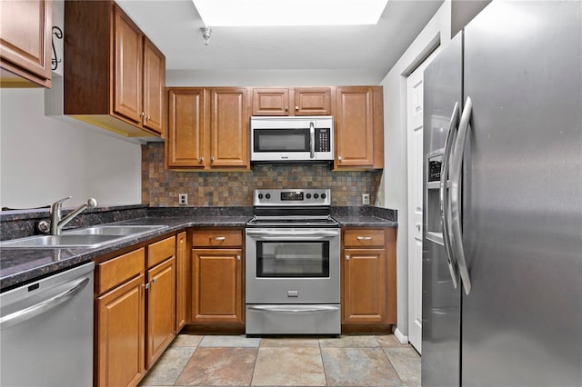 kitchen featuring brown cabinetry, a sink, stone finish flooring, stainless steel appliances, and backsplash