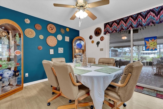 dining area with ceiling fan, an accent wall, baseboards, and wood finished floors