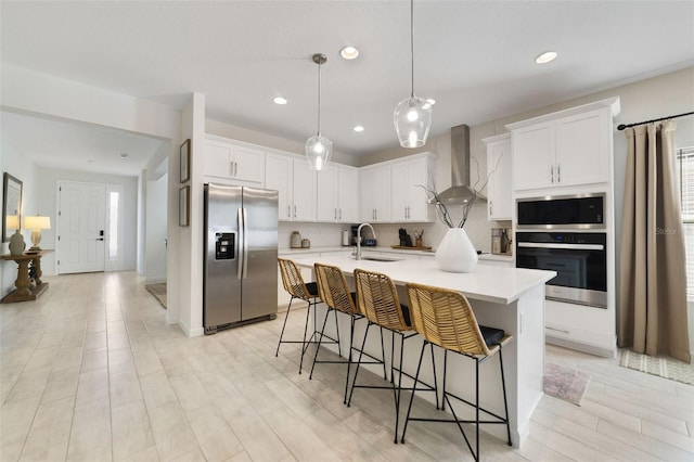 kitchen featuring a sink, light countertops, appliances with stainless steel finishes, and wall chimney range hood