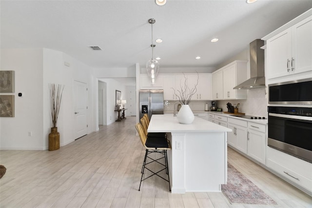 kitchen featuring visible vents, wall chimney exhaust hood, stainless steel appliances, a kitchen bar, and backsplash