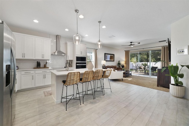 kitchen featuring stainless steel appliances, light countertops, decorative backsplash, open floor plan, and wall chimney exhaust hood