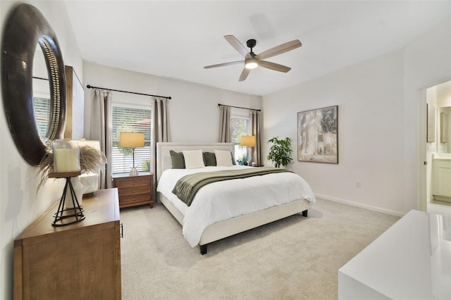 bedroom featuring light carpet, ensuite bath, baseboards, and a ceiling fan