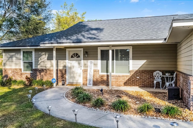 doorway to property featuring roof with shingles and brick siding