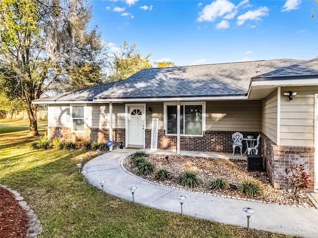 view of front of home with a shingled roof, a front yard, and brick siding