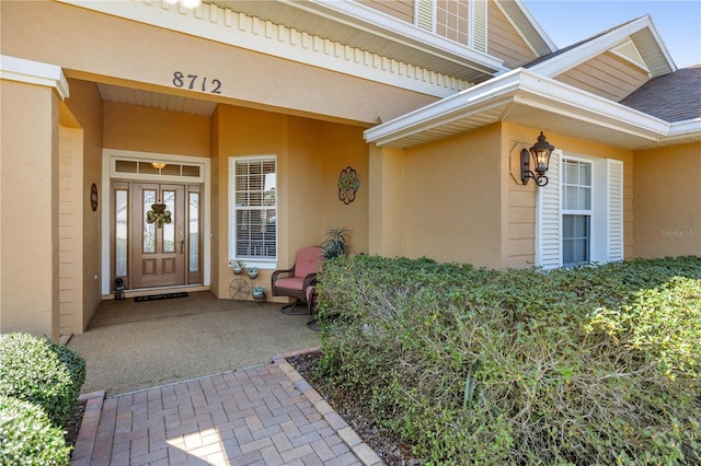 entrance to property featuring a shingled roof and stucco siding