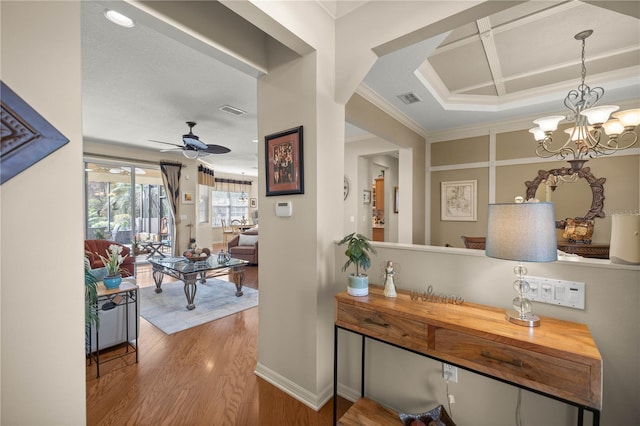 hallway with coffered ceiling, wood finished floors, visible vents, ornamental molding, and an inviting chandelier