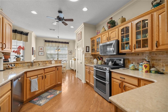 kitchen featuring crown molding, light countertops, appliances with stainless steel finishes, light wood-style floors, and a sink