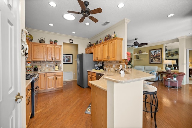 kitchen with a breakfast bar area, a peninsula, a sink, open floor plan, and appliances with stainless steel finishes