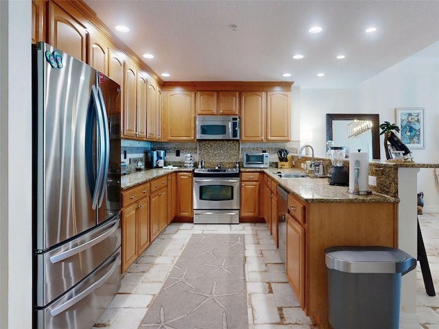 kitchen with a peninsula, appliances with stainless steel finishes, a sink, and light stone counters