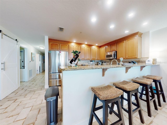 kitchen featuring stainless steel appliances, a peninsula, light stone counters, and a barn door