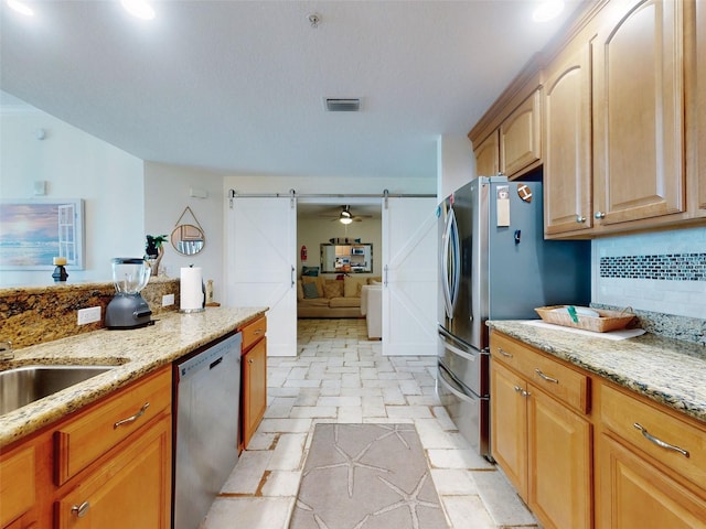 kitchen featuring a barn door, light stone countertops, visible vents, appliances with stainless steel finishes, and decorative backsplash