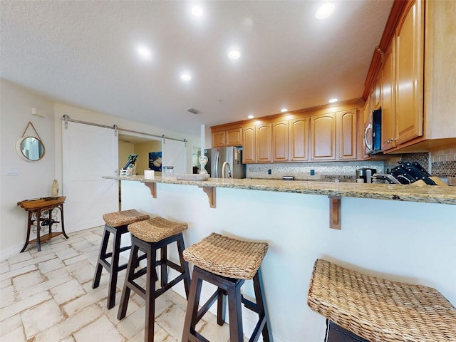 kitchen featuring a peninsula, a barn door, appliances with stainless steel finishes, and tasteful backsplash