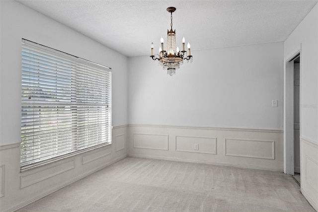 carpeted empty room featuring a textured ceiling, a wainscoted wall, and an inviting chandelier