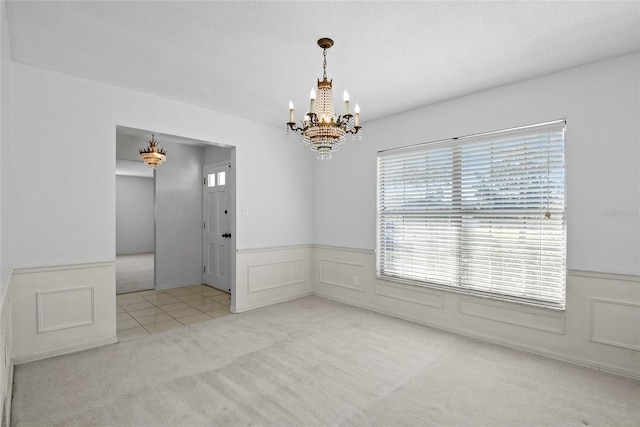 unfurnished room with a textured ceiling, a decorative wall, a wainscoted wall, a notable chandelier, and carpet