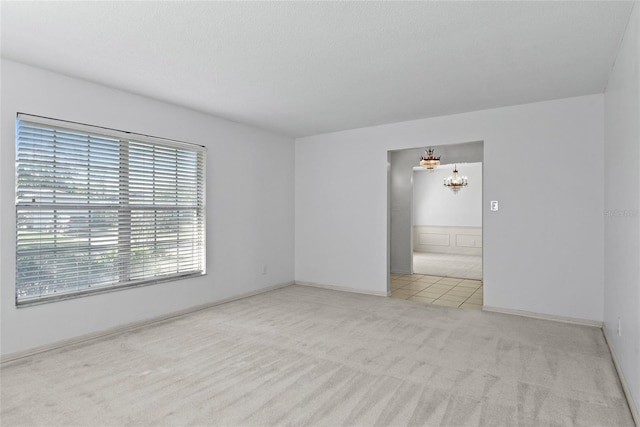 unfurnished room with baseboards, an inviting chandelier, and light colored carpet