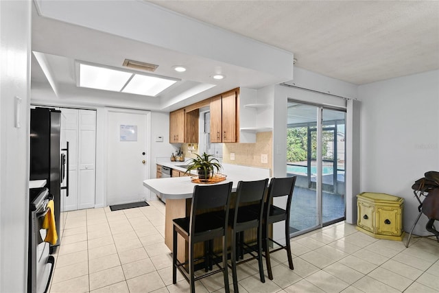 kitchen featuring light tile patterned floors, a peninsula, stove, light countertops, and open shelves