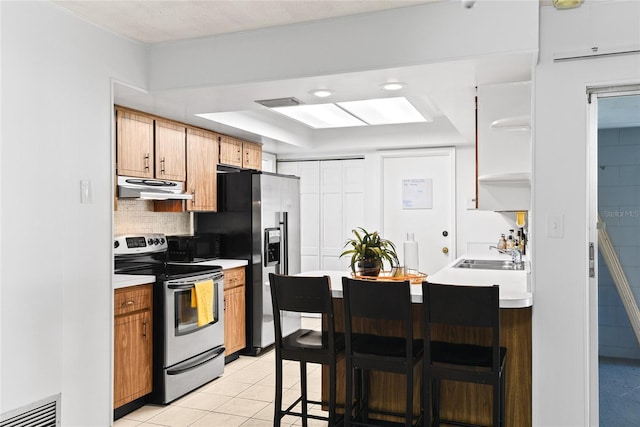 kitchen with under cabinet range hood, a sink, light countertops, appliances with stainless steel finishes, and backsplash