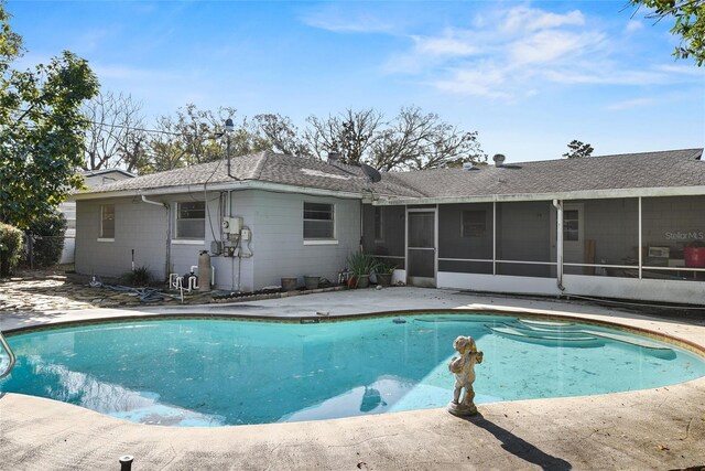 back of property featuring a sunroom, a shingled roof, and an outdoor pool