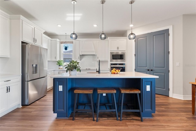 kitchen with stainless steel appliances, premium range hood, a sink, white cabinetry, and a kitchen breakfast bar