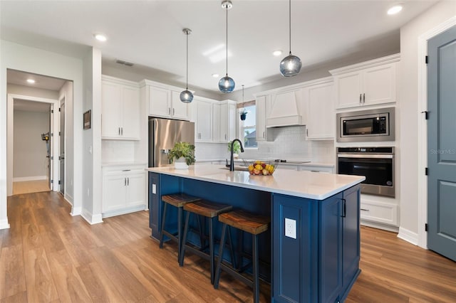 kitchen featuring white cabinets, light countertops, appliances with stainless steel finishes, light wood-type flooring, and custom exhaust hood