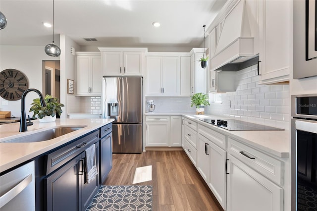 kitchen with stainless steel appliances, premium range hood, a sink, white cabinets, and light countertops