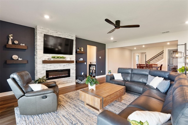 living area featuring ceiling fan, a fireplace, wood finished floors, visible vents, and baseboards