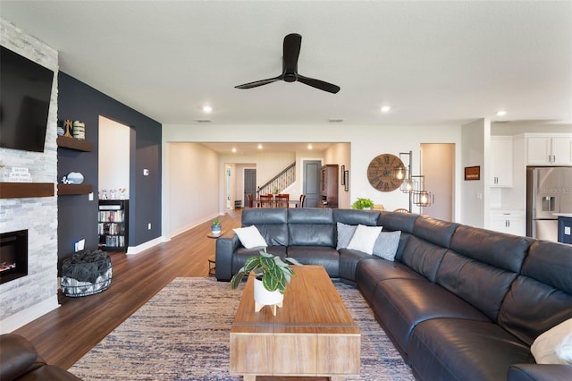 living room with baseboards, dark wood-style floors, stairs, a stone fireplace, and recessed lighting