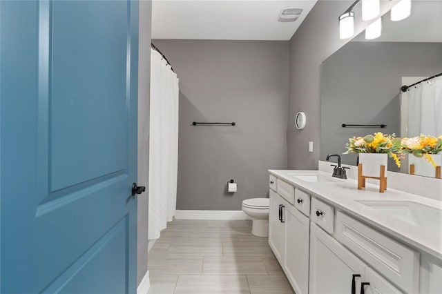 bathroom featuring double vanity, visible vents, toilet, a sink, and baseboards