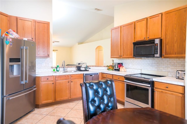 kitchen with light tile patterned floors, lofted ceiling, backsplash, appliances with stainless steel finishes, and a sink